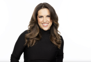 A person with long hair wearing a black turtleneck, smiling against a white background.